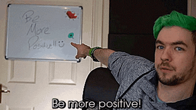 a man with green hair is pointing at a whiteboard that says be more positive