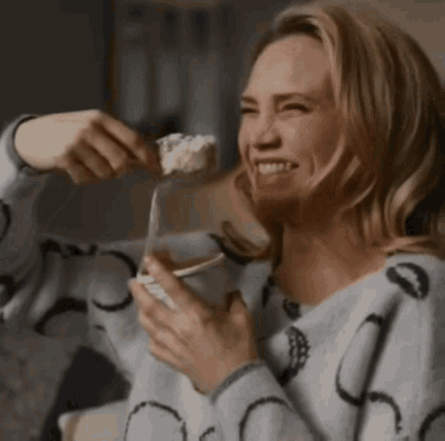 a woman in a sweater is eating ice cream from a spoon