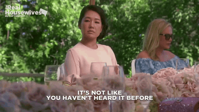 a woman sitting at a table with flowers says it 's not like you haven t heard it before