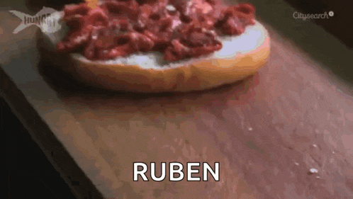 a sandwich with meat on it is on a cutting board and the word ruben is above it