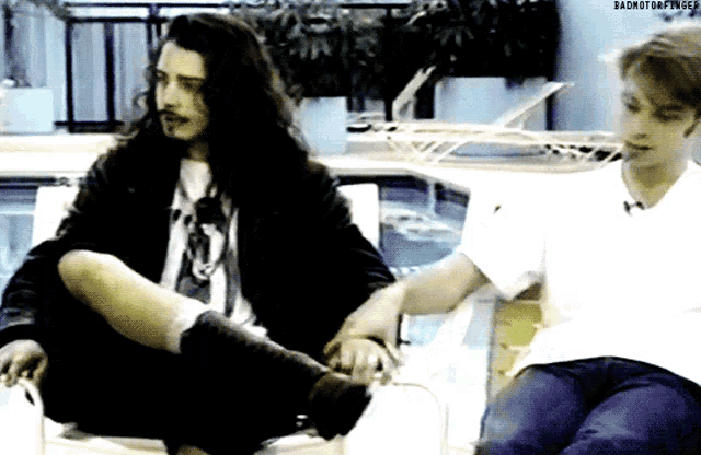 two men are sitting next to each other holding hands and the words badmotorfinger are on the bottom right