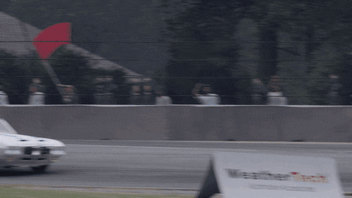 a white car is driving down a race track next to a sign that says master