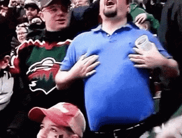 a man in a blue shirt is holding his chest while standing in a crowd of people .