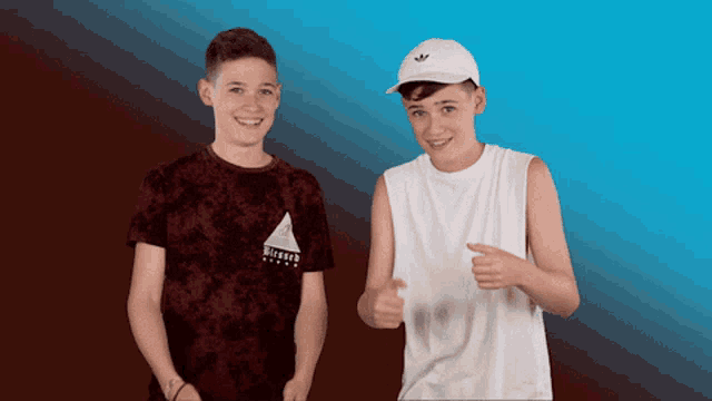 two boys are standing next to each other and one of them is wearing a white hat with adidas on it