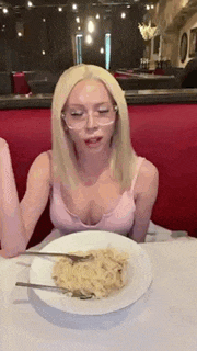 a woman in a pink tank top is sitting at a table with a plate of pasta and forks .
