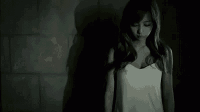 a woman in a white tank top is standing in a dark room with a shadow on the wall .