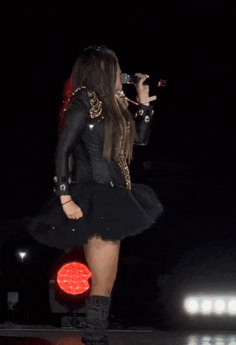 a woman in a black dress and leather jacket stands on a stage with her fist in the air