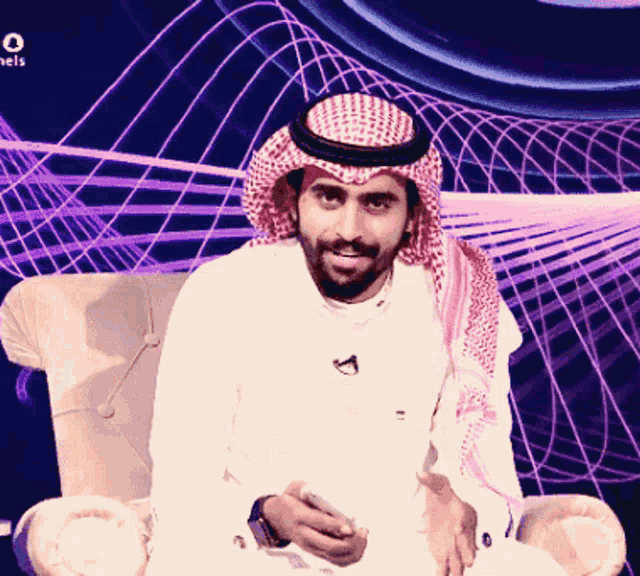 a man wearing a head scarf is sitting in a chair with a purple background