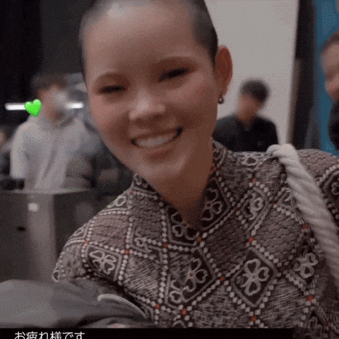 a woman with a shaved head is smiling and wearing a patterned shirt with flowers on it