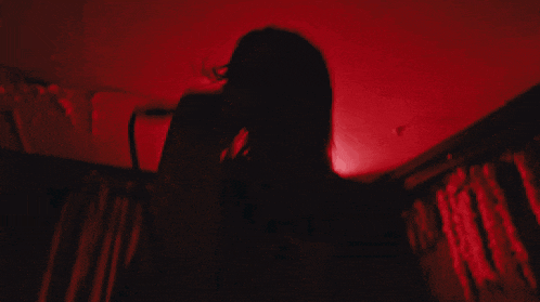 a woman is singing into a microphone in a dark room with red lights behind her