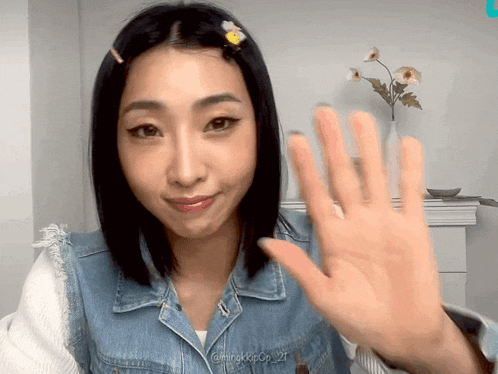 a woman in a denim jacket waves her hand in front of a vase with flowers