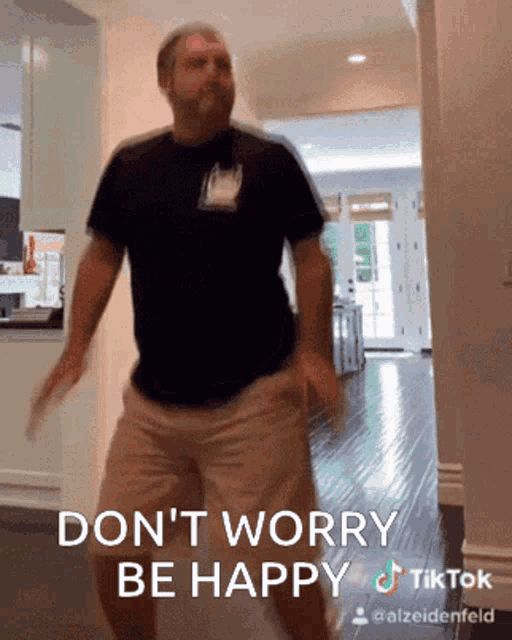 a man in a black shirt and khaki shorts is dancing in a hallway with the caption " don t worry be happy "