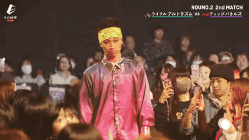 a man in a pink shirt stands in front of a crowd and the words round 2 2nd match are on the bottom