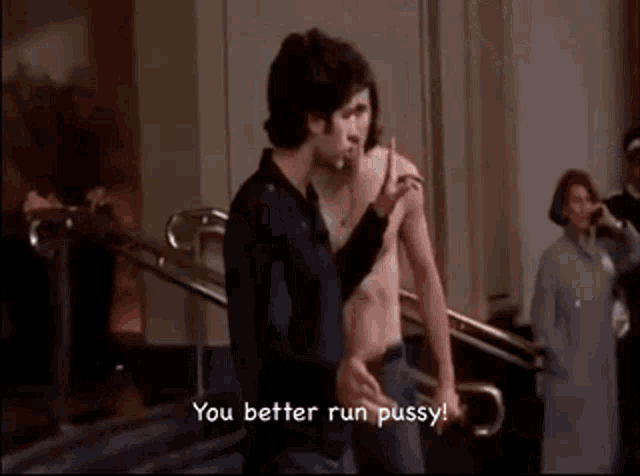two shirtless men are standing next to each other and one of them is smoking a cigarette .