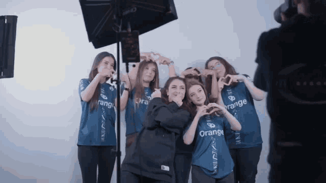 a group of girls wearing orange shirts are making hearts with their hands