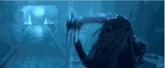 a person is standing in a dark room with their arms outstretched and a blue background .
