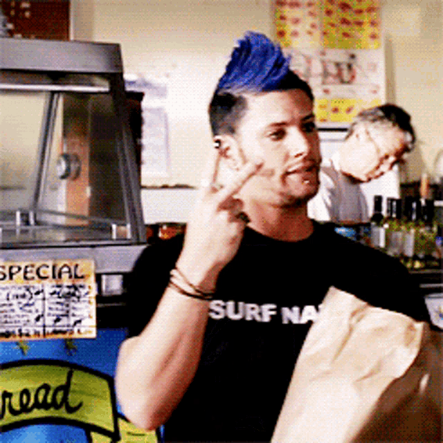 a man with a blue mohawk is wearing a black shirt that says surf nation