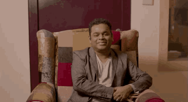 a man in a suit sits in a chair with his hands on his hips
