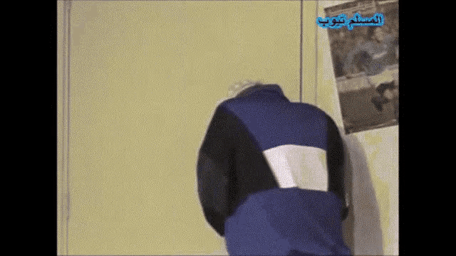 a man in a blue jacket is standing in front of a wall with arabic writing