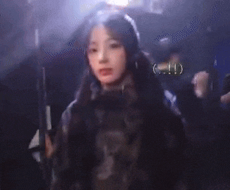 a woman with long hair is standing in front of a crowd of people in a dark room .
