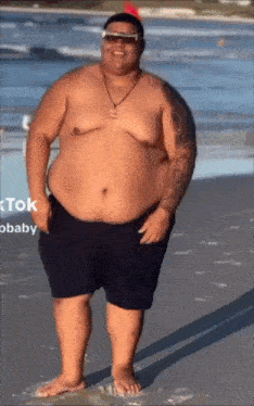 a man with a very large belly is standing on a beach .