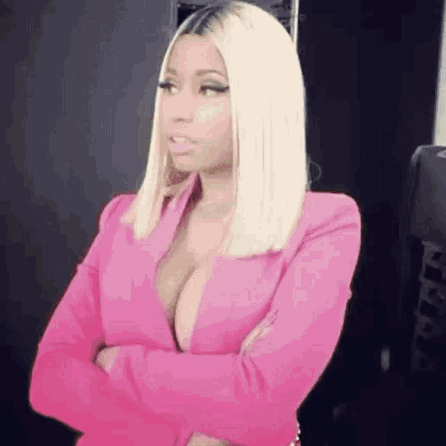 a woman in a pink jacket with her arms crossed is looking at the camera .