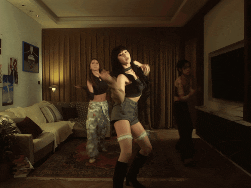 three women are dancing in a living room in front of a flat screen tv