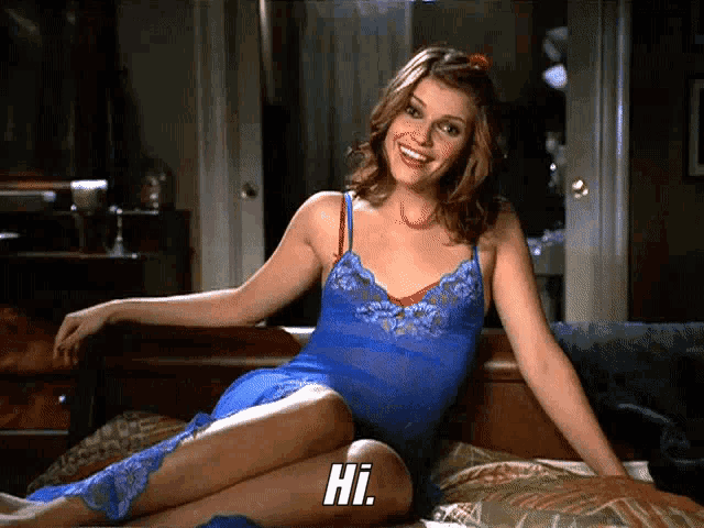 a woman in a blue dress sits on a bed with the word hi written on the bottom
