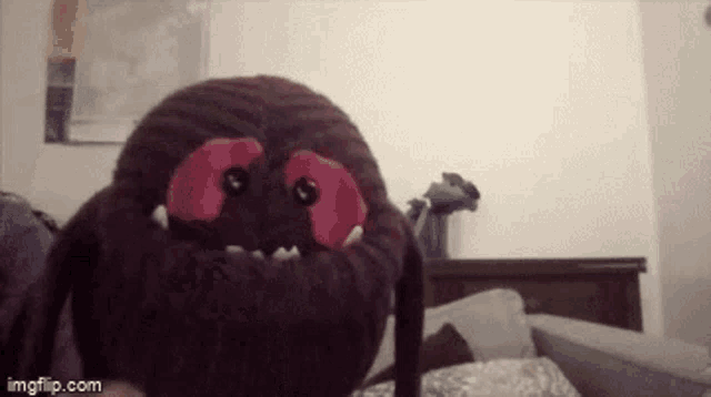 a stuffed spider is sitting on a bed and looking at the camera .