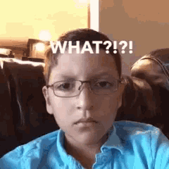 a young boy wearing glasses and a blue shirt is sitting on a couch and making a face .