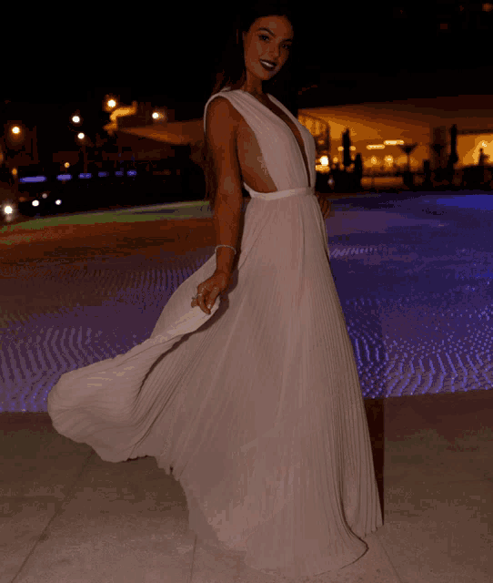 a woman in a long white dress is standing in front of a pool