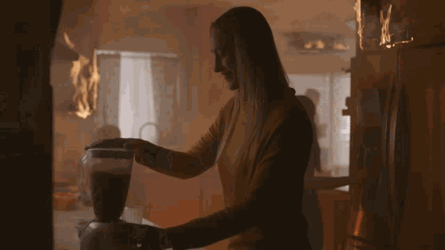 a woman is using a blender in a kitchen with a fire behind her