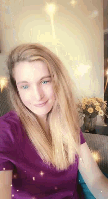 a woman in a purple shirt taking a selfie with a vase of flowers in the background
