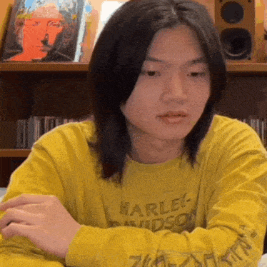 a young man wearing a yellow harley davidson t-shirt is sitting at a table .