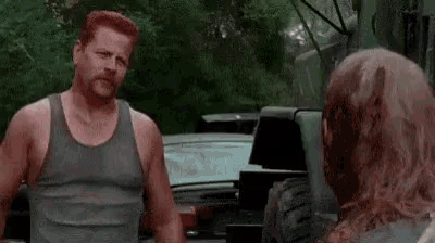 a man in a tank top is standing next to a dead man .