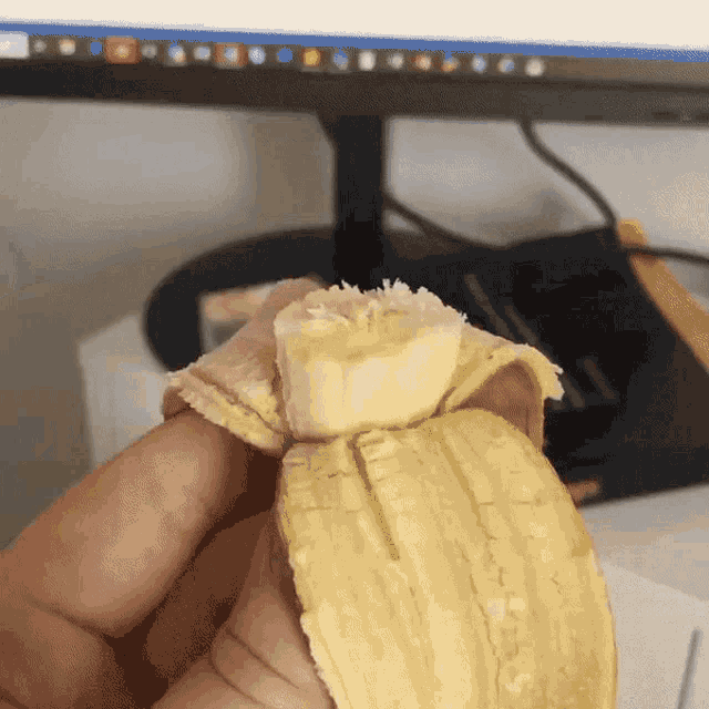 a person is holding a peeled banana in front of a computer screen