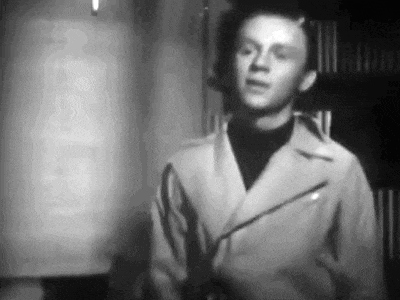 a black and white photo of a man in a jacket standing in front of a lamp .