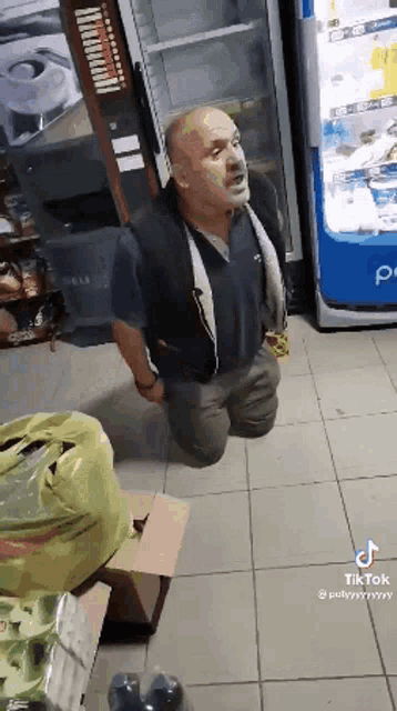 a man is kneeling on the floor in front of a pepsi machine in a store .