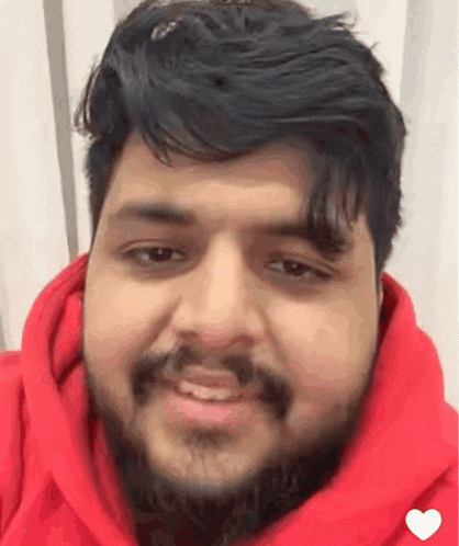 a man with a beard is smiling and wearing a red hoodie .