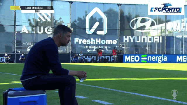 a man sits on a cooler on a soccer field in front of hyundai and fresh home signs