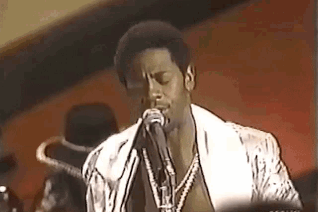 a man singing into a microphone while wearing a white jacket