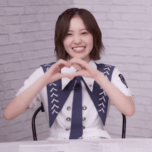 a woman making a heart shape with her hands in front of a brick wall