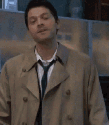 a man in a trench coat and tie is standing in a room with his eyes closed .