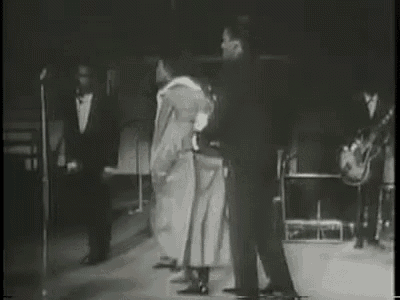 a black and white photo of a group of men standing on a stage .