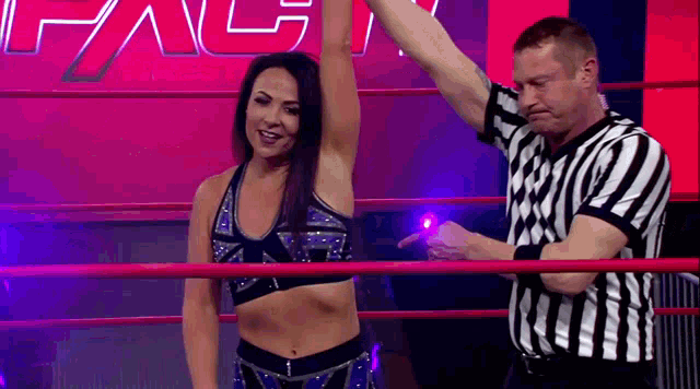 a woman is standing in a wrestling ring with her arm in the air while a referee points at her .