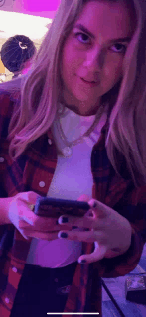 a woman in a plaid shirt holds a cell phone