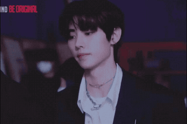 a young man wearing a suit and a necklace with the words ind be original on the bottom