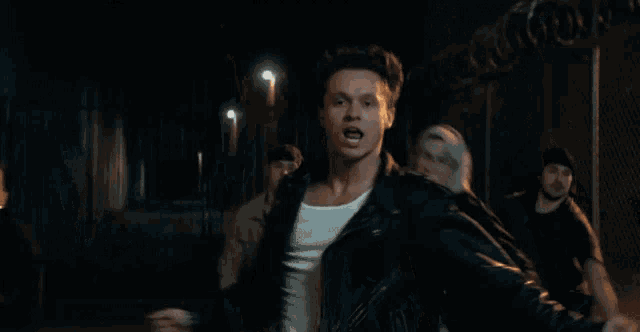 a man in a white tank top and a leather jacket is dancing in a crowd .
