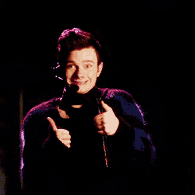 a young man is holding a microphone and smiling in the dark
