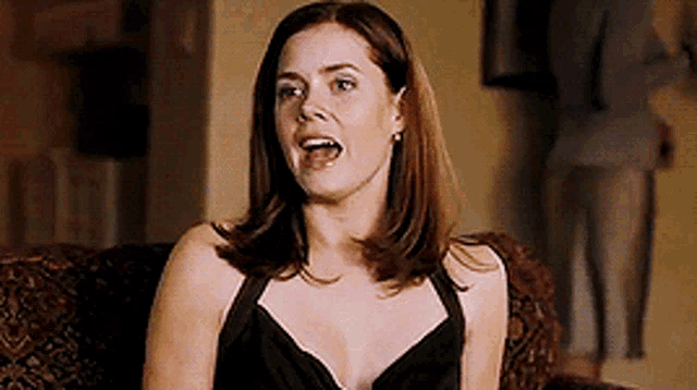 a woman in a black dress is sitting on a couch with her mouth open